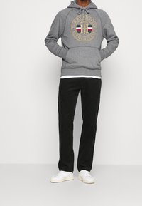 Felpa grigia con un logo rotondo, abbinata a pantaloni neri in velluto a coste e sneakers bianche. Il tessuto ha una texture morbida e un design semplice.