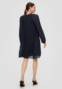 Marineblaues plissiertes Kleid mit langen Ärmeln, rundem Ausschnitt und fließendem Stoff. Es verfügt über ein strukturiertes, transparentes Material und endet oberhalb der Knie.