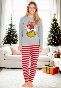 Maglietta grigia a maniche lunghe con grafica del Grinch e testo, abbinata a pantaloni da pigiama a righe rosse e grigie, esposta in un accogliente ambiente interno.