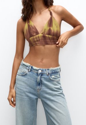 Femme portant un crop top halter tie-dye marron et vert et un jean bleu clair délavé taille haute sur fond blanc.