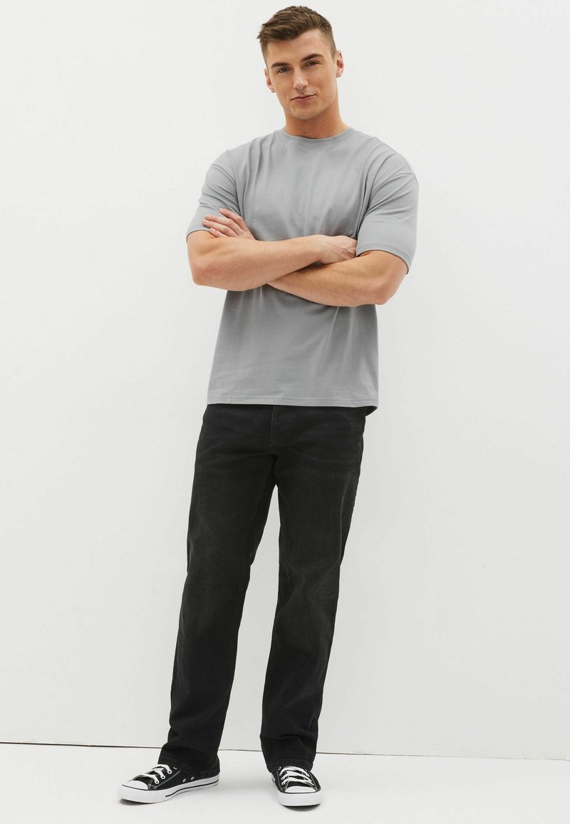 Tricou gri cu guler rotund, asortat cu blugi negri din denim. Tricoul are mâneci scurte, iar blugii au un design cu picior drept și sunt purtați cu adidași negri.