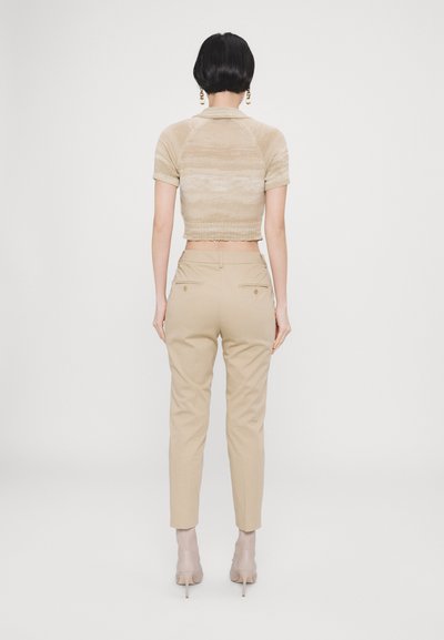Beige kortermet strikket polo med korte ermer, kombinert med skreddersydde beige bukser med slank passform og baklommer. Nøytrale hæler.