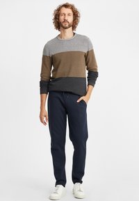 Stickad tröja med grå, brun och svarta horisontella ränder, rundad halsringning; ihop med mörk marinblå sweatshirtbyxor och vita sneakers.