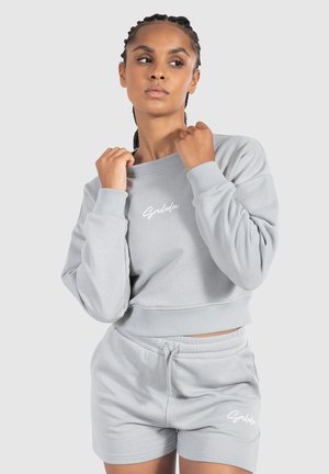 Light grey cropped sweatshirt with ribbed cuffs and waistband, featuring "Smiledex" logo in white. Paired with matching grey shorts.