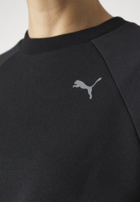 Felpa nera con collo a costine, maniche raglan e un piccolo logo grigio Puma sul petto. Texture del tessuto liscia.