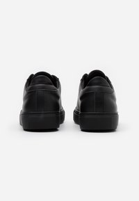 Zapatillas deportivas de cuero negro con textura suave, tacón redondeado y suela de goma. Presentan costuras mínimas y no tienen marcas visibles.