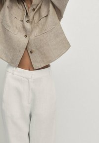 Linned cropped jakke i lys beige med to frontlommer og træknapper, kombineret med hvide lige ben bukser.