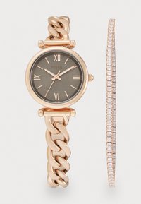 Montre en or rose avec bracelet à maillons, cadran gris foncé, chiffres romains, accompagnée d'un bracelet mince et scintillant sur fond blanc.