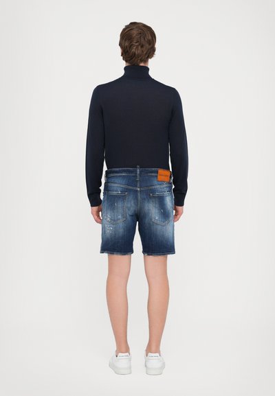 Marineblauer Rollkragenpullover mit taillierter Passform, kombiniert mit ausgewaschenen blauen Denim-Shorts. Weiße Sneaker mit einem cleanen Design.