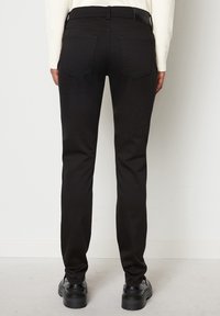 Jeans neri con una vestibilità slim, dotati di vita standard e tasche posteriori. Il tessuto ha una texture liscia e dettagli minimi.
