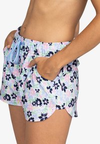 Shorts de bain floraux en couleurs pastel avec un cordon de serrage bleu, des poches latérales et un ourlet arrondi arborant un petit logo en bas à gauche.