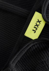 Zwarte stof met een geribbelde textuur, voorzien van een felgele label met de inscriptie "JJXX." De randen lijken afgewerkt en glad te zijn.