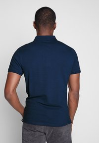 Polo shirt bleu marine à manches courtes et col. Tissu en coton lisse, avec un design arrière épuré et des accents de couture contrastés.