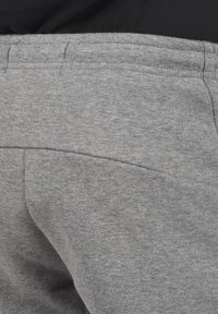 Grå bomulds sweatpants med en glat tekstur, en baglomme og synlige syninger langs taljen og sømmene.