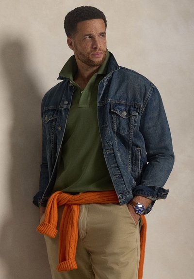 Τζιν μπουφάν με μπλε ξεθώριασμα, πράσινο πόλο πουκάμισο και μπεζ παντελόνι. Πορτοκαλί πλεκτό πουλόβερ δεμένο γύρω από τη μέση. Ασημένιο ρολόι στον καρπό.