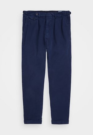 Navy chinos made from cotton, featuring a straight-leg cut, front pleats, button closure, and rolled cuffs. Smooth texture with minimal design.