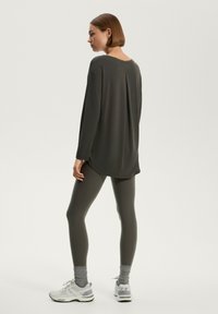 Maglietta a maniche lunghe grigio scuro con scollo rotondo, abbinata a leggings coordinati. Scarpe da ginnastica nere e grigie con dettagli di ammortizzazione.