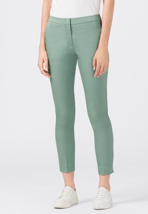 Grønne skræddersyede bukser lavet af glat stof, med en tætsiddende pasform og kort længde. Kombineret med hvide sneakers for et afslappet look.