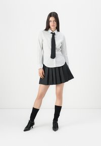 White and gray striped shirt with a black tie, paired with a black pleated skirt. Features black knee-high socks and pointed black heels.