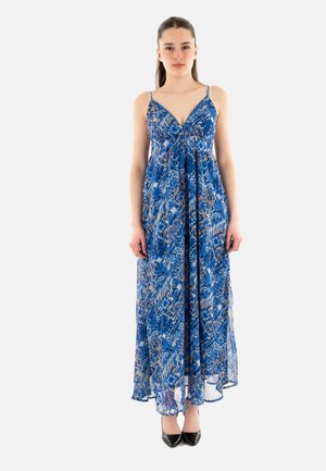 Abito maxi blu con un design a fantasia. Presenta spalline sottili e un tessuto fluido e trasparente. Indossato con tacchi neri.