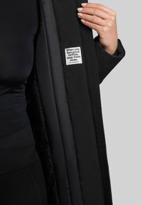 Sort isoleret jakke med en glat overflade og en varm foring. Indvendig label indeholder tekst. Nærbillede af stof og design detaljer.