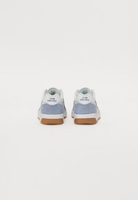 Blå ruskinnsneakers med hvite detaljer, runde snørebånd og en gummisåle. Har "new balance" merkevare på hælen. Enkel, lavt glidende design.