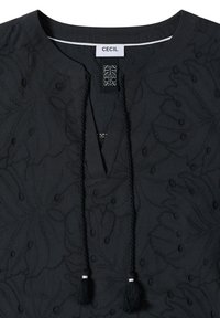 Haut noir avec broderie florale, encolure en V avec liens à pompons, encolure ronde et étiquettes de la marque cousues à l'intérieur du col.