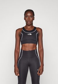 Svart atletisk crop top med racerback-design och framträdande logotyp. Matchas med högmidjade, kroppsnära svarta leggings med kontrasterande sömmar.