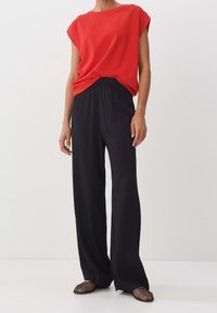 Rotes Kurzarmoberteil mit lockerem Schnitt, kombiniert mit weit geschnittenen schwarzen Hosen und schwarzen Netz-Slippern. Einfaches Design, glatte Textur.