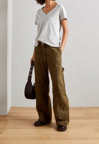 Grijs V-hals T-shirt, losse kaki cargobroek met knopen aan de voorkant, zakken aan de zijkant en brede pijpen, gecombineerd met een kleine zwarte handtas en donkere schoenen.