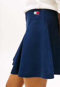 Navy blue flared skirt made of textured fabric, featuring a small embroidered Tommy Jeans logo on the waistband.