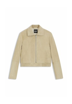 Cropped beige suede jacket with a collared neck, front zipper, and ribbed hem. Features diagonal seam details and subtle logo accent.