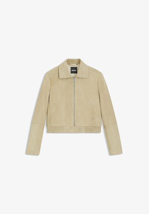 Veste courte en daim beige avec col, fermeture éclair à l'avant et ourlet côtelé. Présente des détails de coutures diagonales et un accent discret de logo.