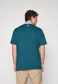 Teal kortermet polo med lys blå krage og logo på baksiden av nakken. Laget av bomull med en jevn tekstur.