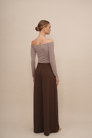Off-the-shoulder, lavender top with long sleeves paired with high-waisted, wide-leg brown trousers. Smooth fabric, minimal detailing.