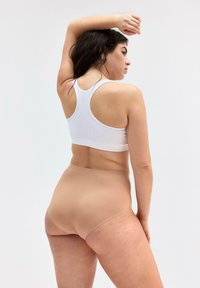 Lätt vit ribbad tanktop och nude högmidjade underkläder, som visar en slät, sömlös design med en subtil lyster.