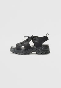 Black athletic sandals featuring a mix of textured fabric and rubber. Open design with prominent grooves in the sole and adjustable laces.
