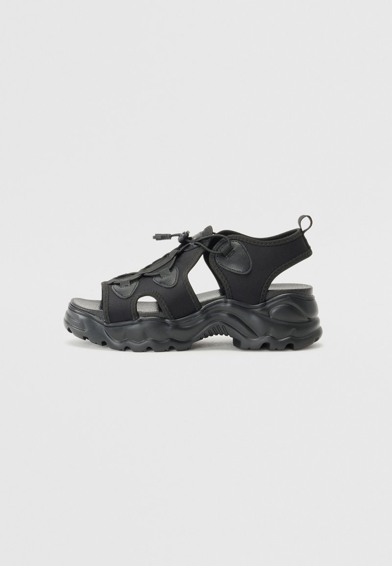 Black athletic sandals featuring a mix of textured fabric and rubber. Open design with prominent grooves in the sole and adjustable laces.