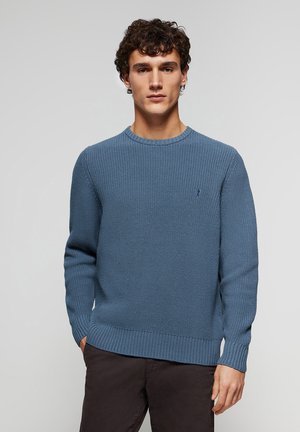 Suéter de punto en suave azul, con cuello redondo, puños y dobladillo de canalé, y un pequeño logotipo destacado en el pecho.