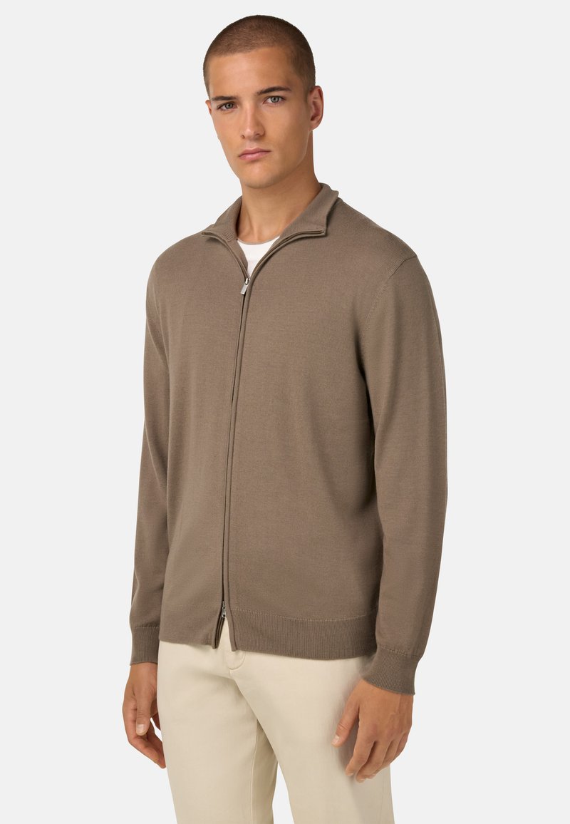 Kergepruunist tõmblukuga kardigan, kudumise tekstuuriga, millel on tõusnud krae ja soonikvarrukad. Kandmine valge särgi peal.