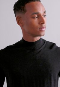 Pull en col roulé noir en tissu lisse et léger. Dispose d'un col haut et d'une coupe ajustée avec des coutures minimales.