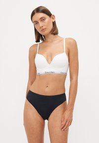 Witte bralette met lichte padding, plunge halslijn en dunne bandjes. Zwarte hooggesneden onderbroek met een gladde textuur en een minimalistisch ontwerp.