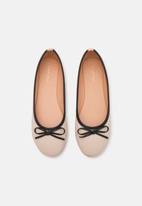 Ballerinaskor i ljusbeige med svart kant och rosettdetalj. Slät ovandel, rund tå och vadderad sula.