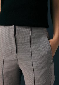 Pantalons à carreaux noirs et beiges, offrant une coupe ajustée, des poches avant et des lignes épurées, complétés par un haut texturé noir.
