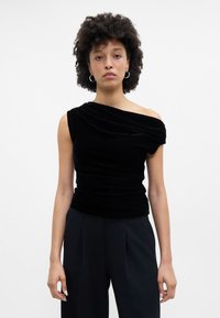 Μαύρη βε�λούδινη τοπ με ένα ώμο, με υφή που πέφτει και εφαρμοστή σιλουέτα. Συνδυασμένο με ψηλόμεσες μαύρες παντελόνες.