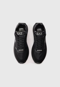 Zapatillas deportivas negras con parte superior de malla y acentos de ante. Presenta cordones, un logo en la lengüeta y una suela de goma texturizada.