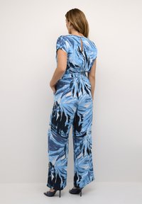 Jumpsuit azul y blanco con un estampado, mangas cortas, detalle de ojal en la espalda y piernas anchas; acentuado con una cintura ceñida.