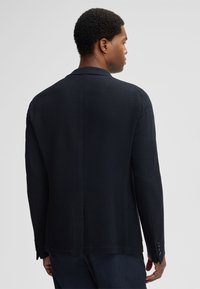 Strukturierter dunkelblauer Blazer mit taillierter Passform, Reverskragen und vier Knöpfen an jedem Ärmel. Verfügt über eine Schlitze am Rücken.