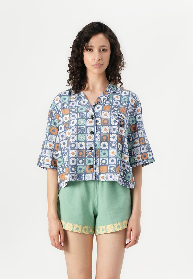 Cropped shirt features a blue and multi-colored floral pattern with short sleeves and six buttons. Paired with textured mint green shorts.