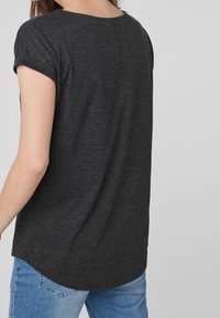 Kortærmet, mørkegrå T-shirt med rund hals og blød tekstur, med en buet kant bagpå, parret med lyseblå jeans.